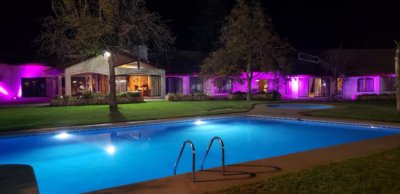 Piscina y jardín de Pirque iluminados de noche con luz púrpura